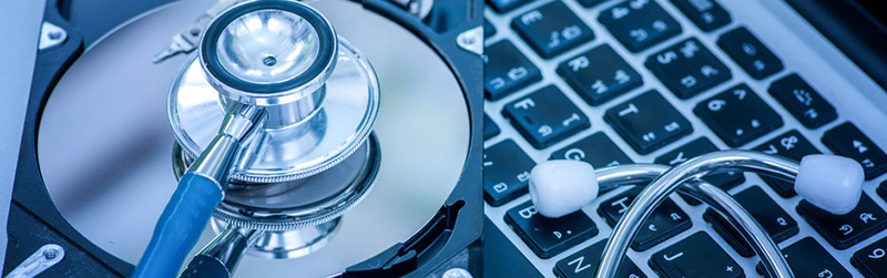Stethoscope placed on a hard disk platter next to a laptop keyboard, symbolizing computer diagnostics and repair.