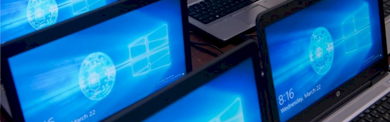 Multiple laptops displaying Windows login screens arranged on a desk.