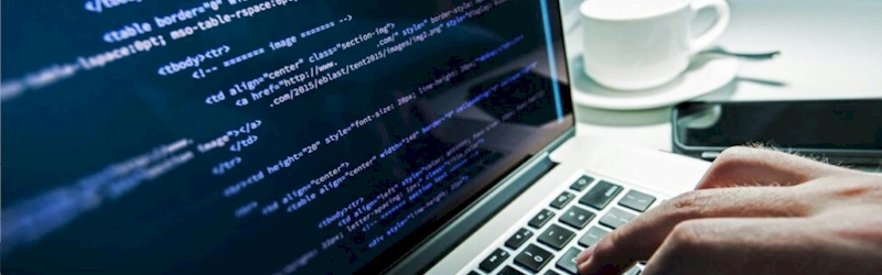 Laptop screen displaying lines of code with a person typing on the keyboard, representing programming and software development
